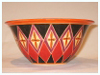 A Bali stoneware wide bowl, decorated with diamond shape geomatric design and glazed with red and black unerglazes on peach background - first view.